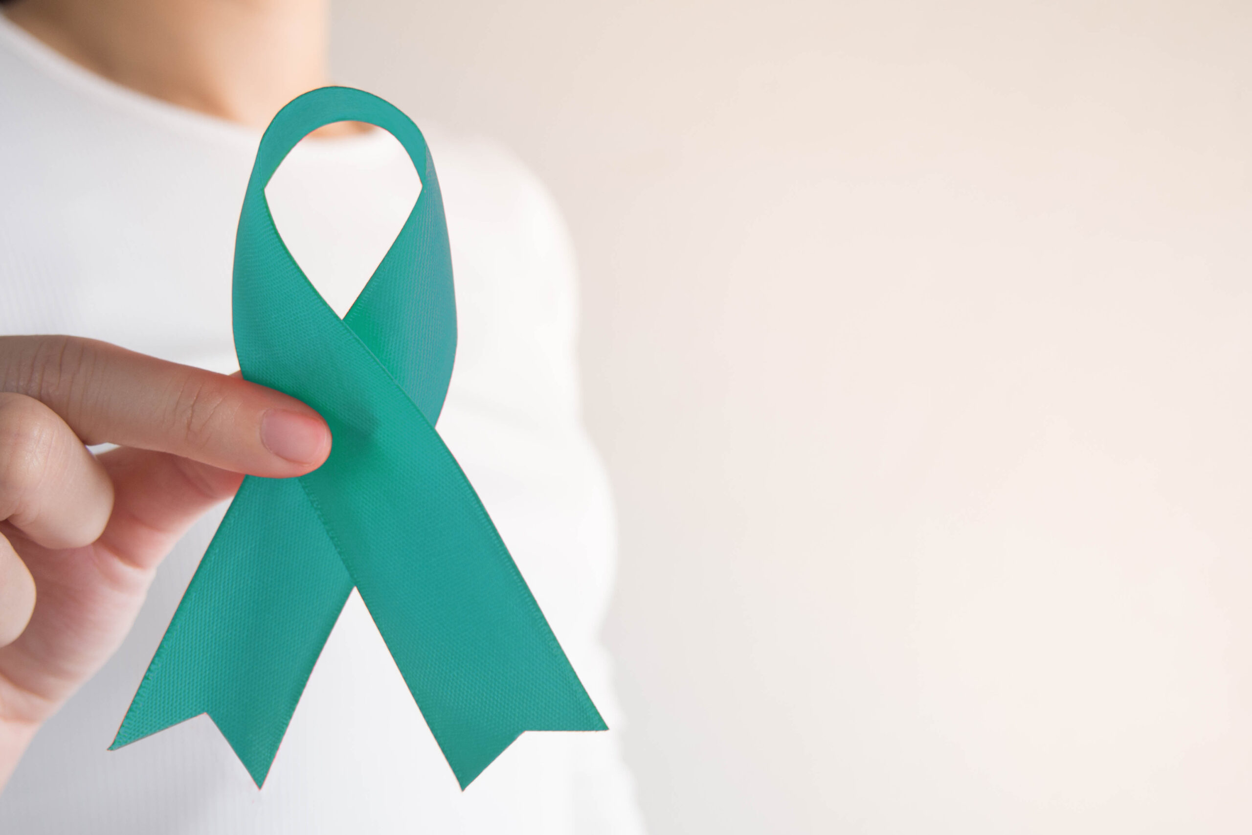 Woman’s hand using pointer finger and thumb to hold a teal ribbon in honor of ovarian cancer awareness